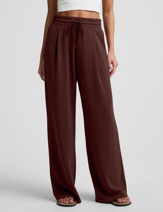 Woman wearing a white cropped tank and brown wide leg pants against a plain background.