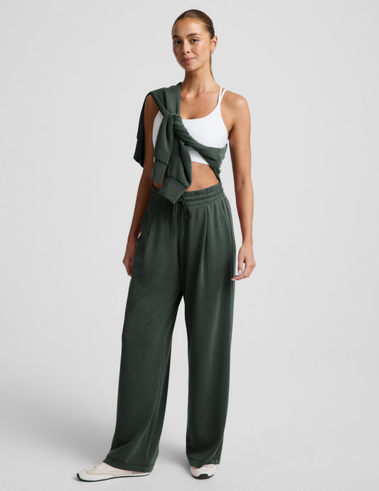 Woman wearing Dark green Luxe Sandwash Double Knit Wide Leg Pant with front pleats, a white sports bra and sweatshirt.