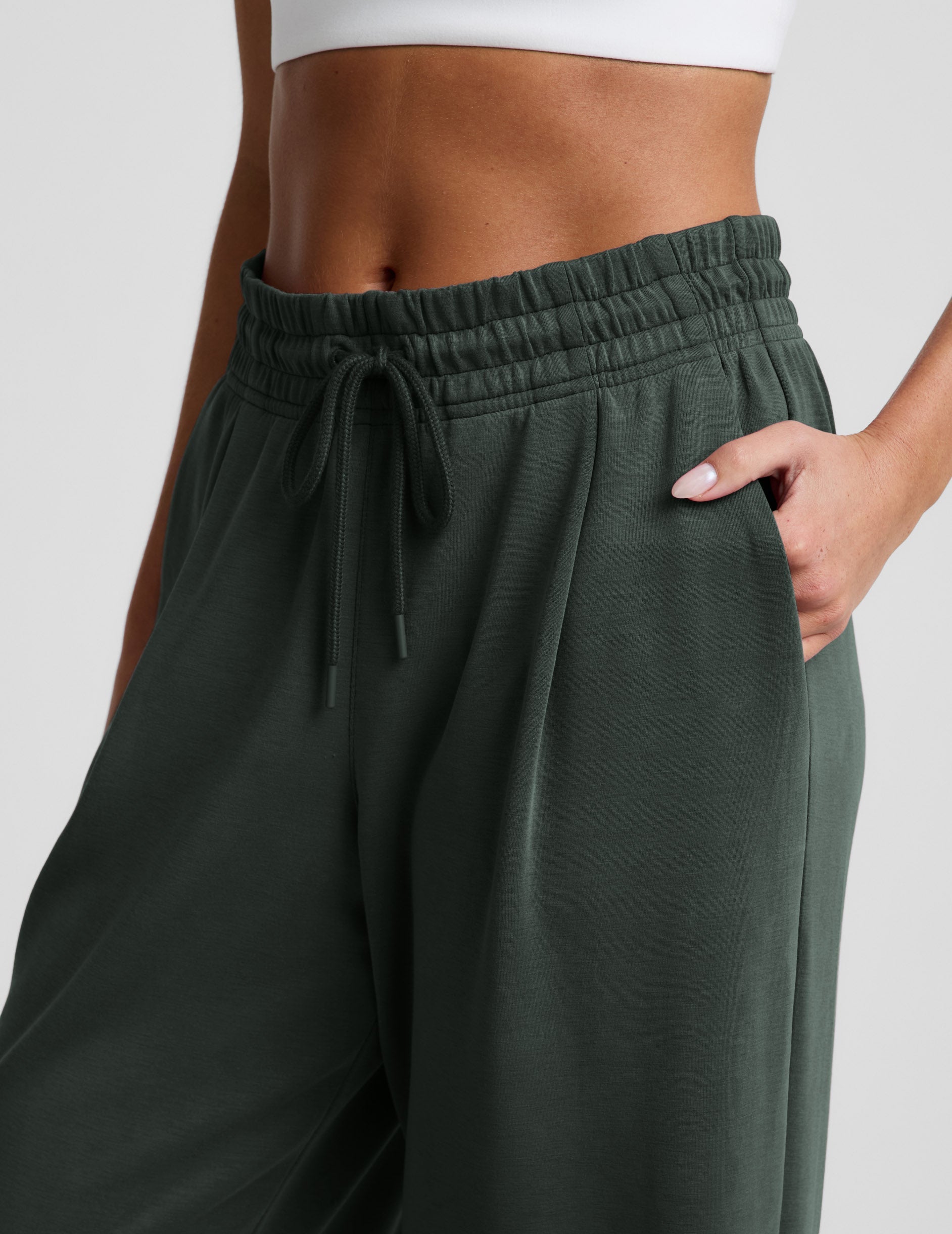 Woman wearing green Luxe Sandwash Double Knit Wide Leg Pant™ with a white sports bra, showing the drawstring waistband.