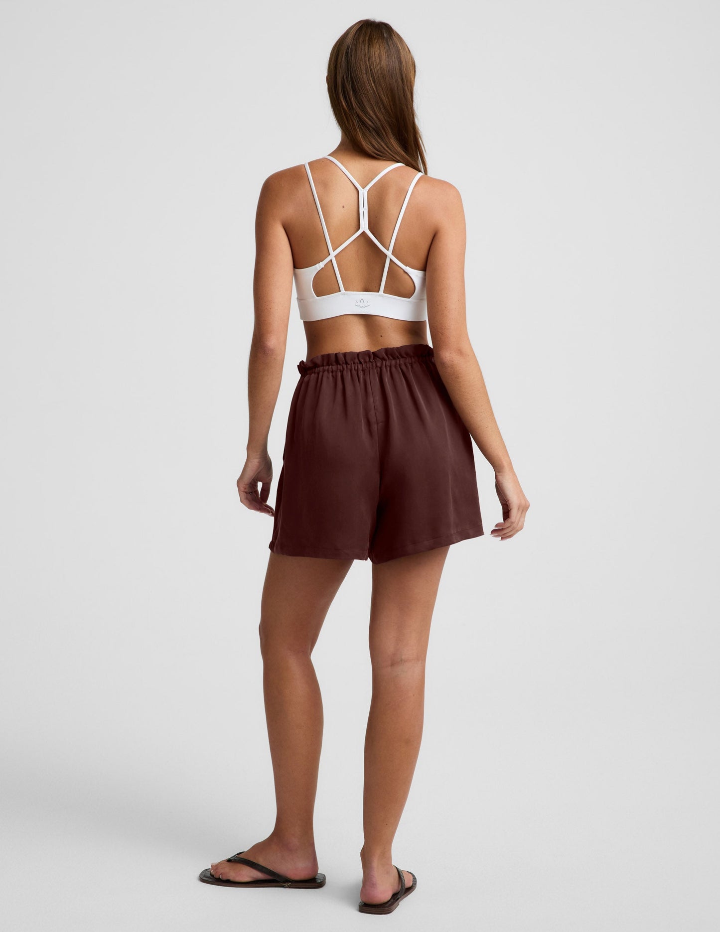 Woman wearing Chocolate SunKissed Cupro Drawstring Short™ from the rear, paired with a white strappy sports bra.