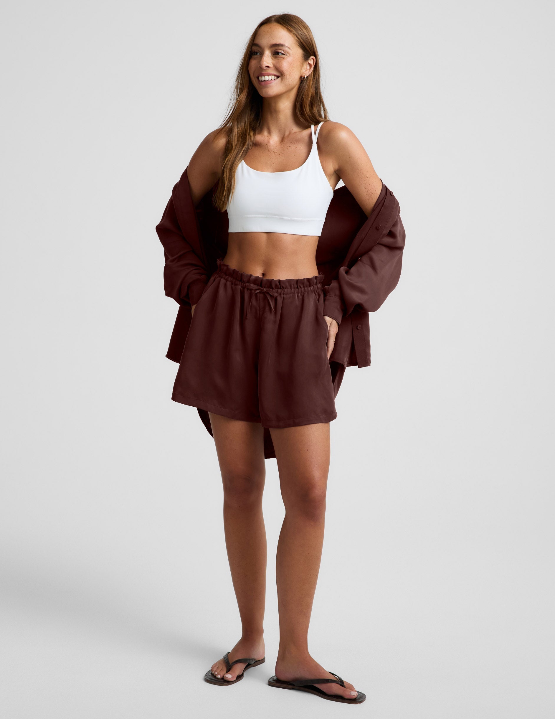 Woman wearing Brown SunKissed™ Cupro Drawstring Short with a high rise, paired with a white sports bra and matching shirt.