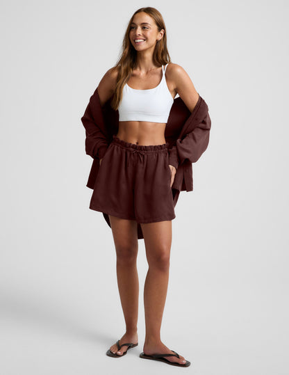 Woman wearing Brown SunKissed™ Cupro Drawstring Short with a high rise, paired with a white sports bra and matching shirt.