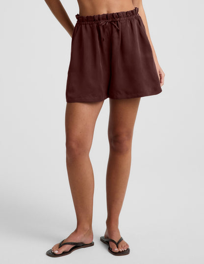 Woman wearing brown SunKissed™ Cupro Drawstring Short with a flared silhouette, paired with dark flip-flops.