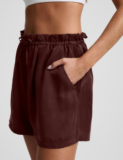 Side profile of woman wearing Mahogany SunKissed™ Cupro Drawstring Short with a white top, featuring a side pocket.