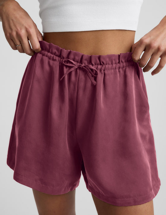 Woman wearing Berry SunKissed Cupro Drawstring Short™ with a high-rise elastic waistband, paired with a white ribbed crop top.