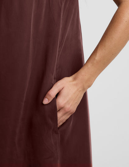 Woman wearing a brown maxi cupro dress against a plain background.