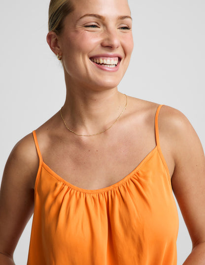 Woman wearing an orange cupro mini dress and brown sandals against a plain background.