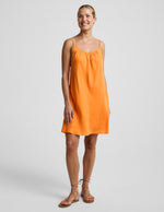 Woman wearing an orange cupro mini dress and brown sandals against a plain background.