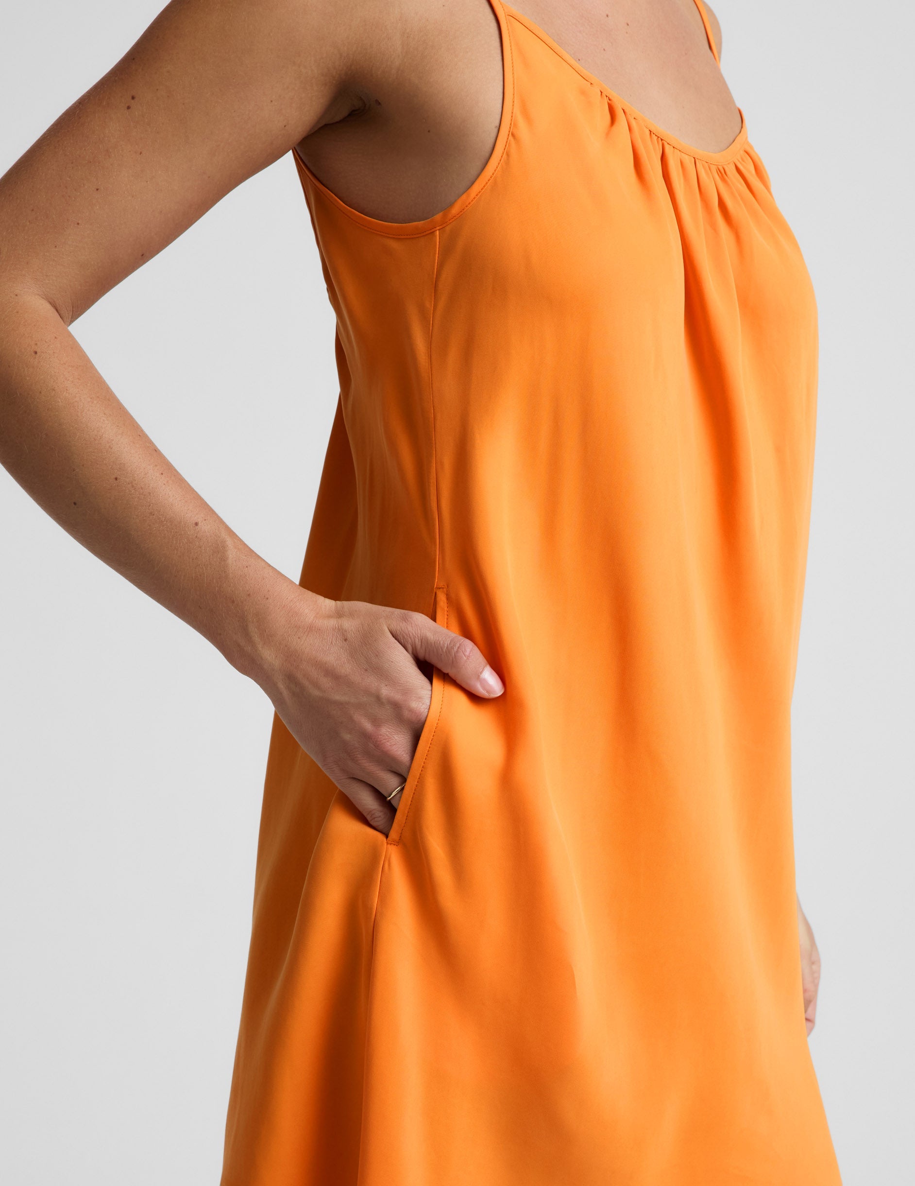 Woman wearing an orange cupro mini dress and brown sandals against a plain background.