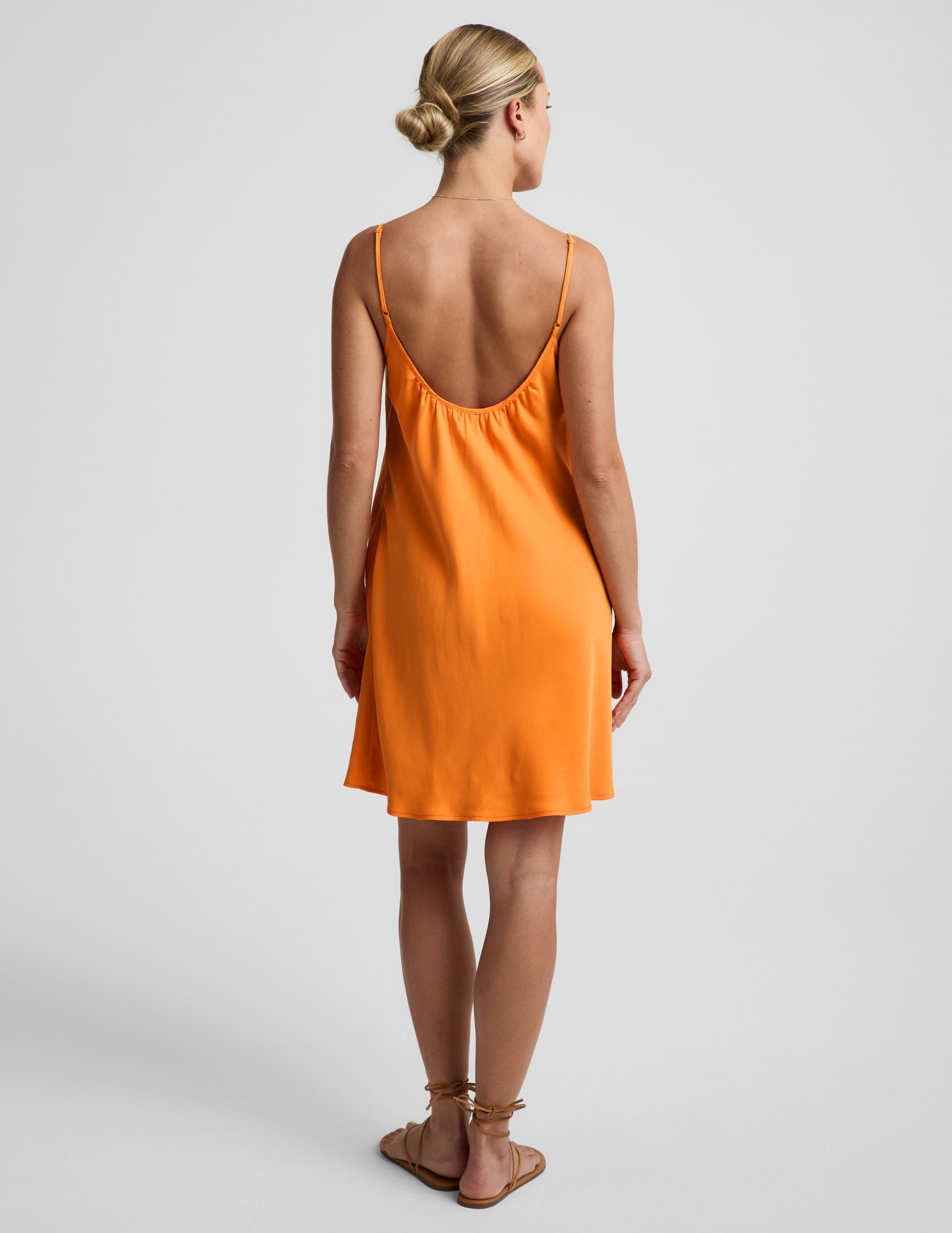 Woman wearing an orange cupro mini dress and brown sandals against a plain background.