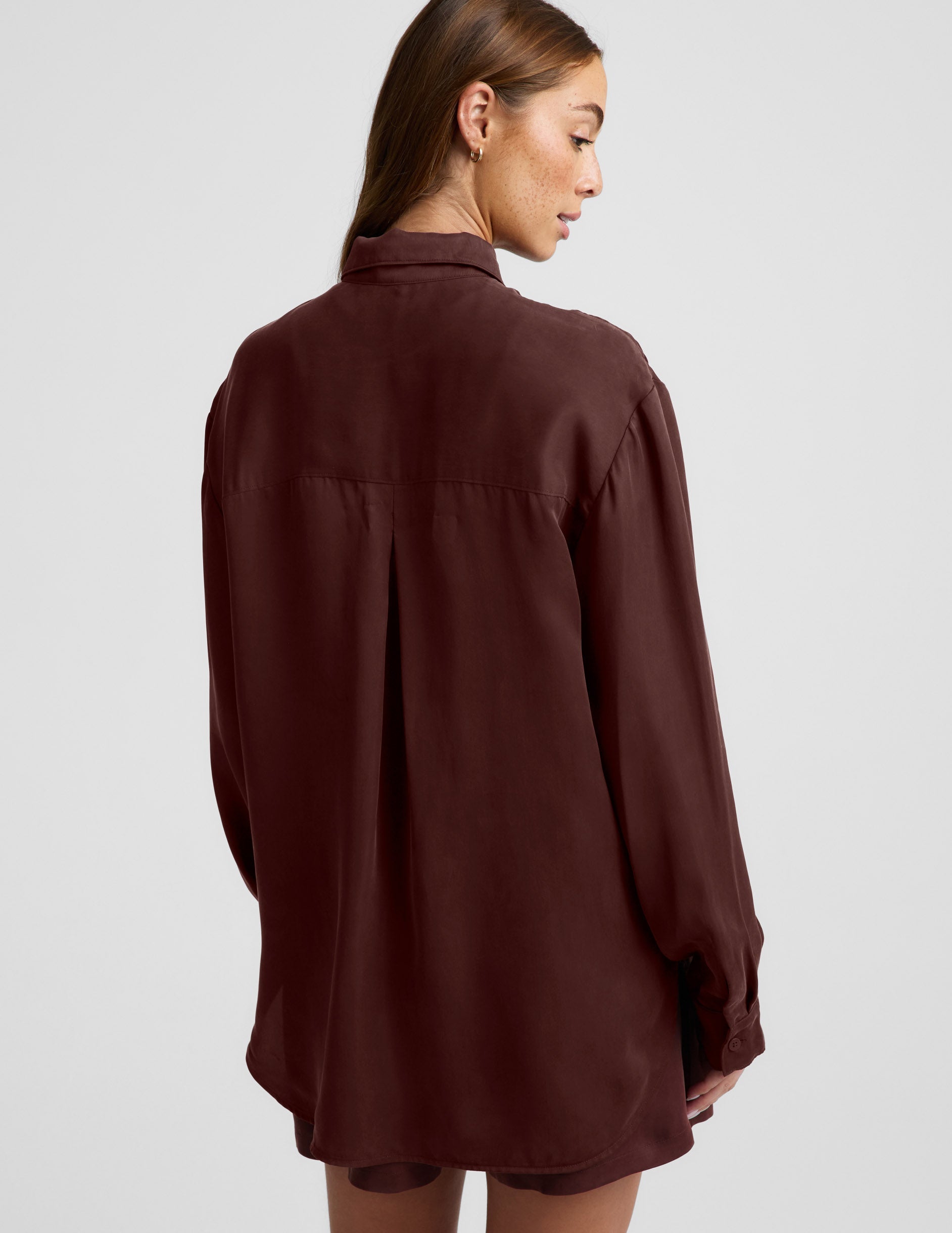 Woman wearing a brown button up shirt and shorts against a plain background.