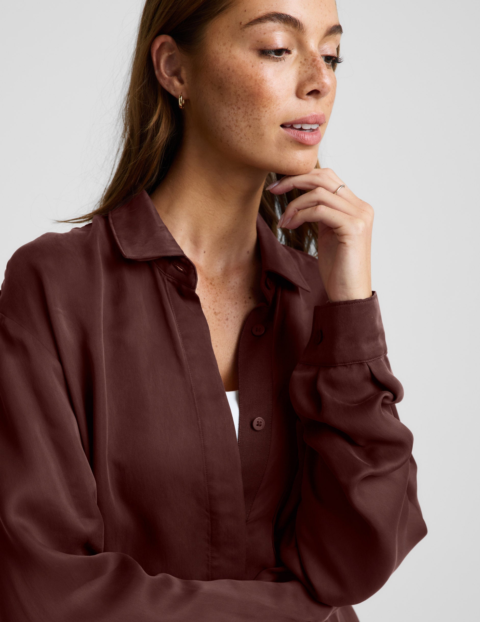 Woman wearing a brown button up shirt and shorts against a plain background.