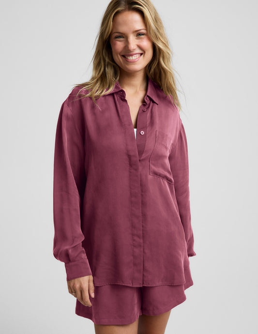 Woman wearing a purple button down shirt and shorts against a plain background.