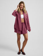 Woman wearing a purple button down shirt and shorts against a plain background.