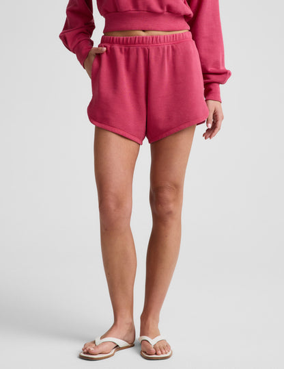 Woman wearing Pink Fade Out Mid-Rise Short™ with curved hems, paired with a matching sweatshirt and white flip-flops.
