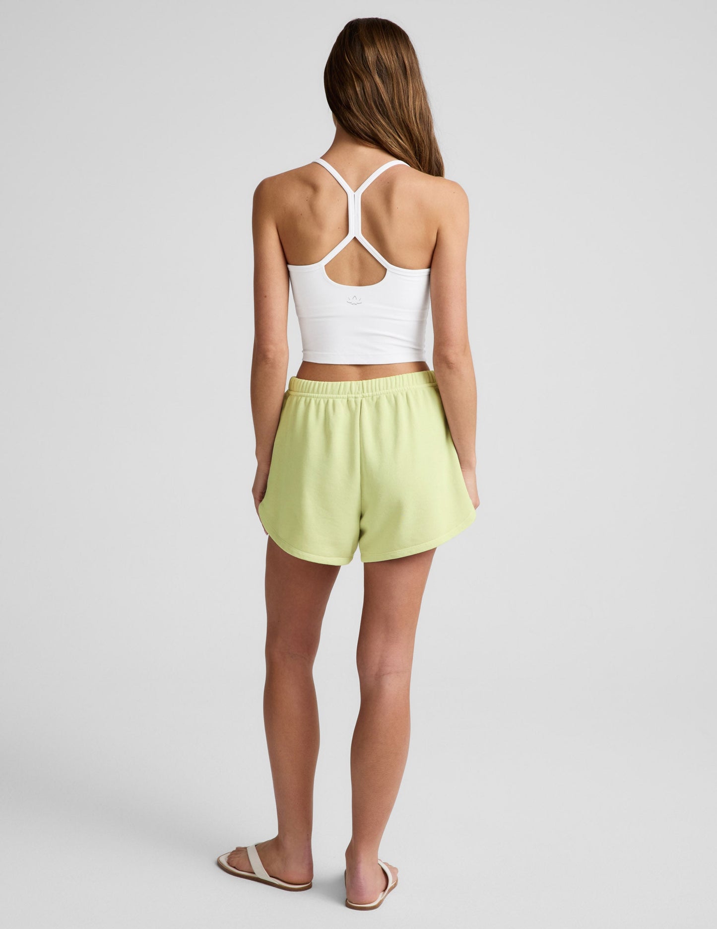 Rear view of woman wearing yellow Fade Out Mid-Rise Short™ with a curved hem, paired with a white crop top.
