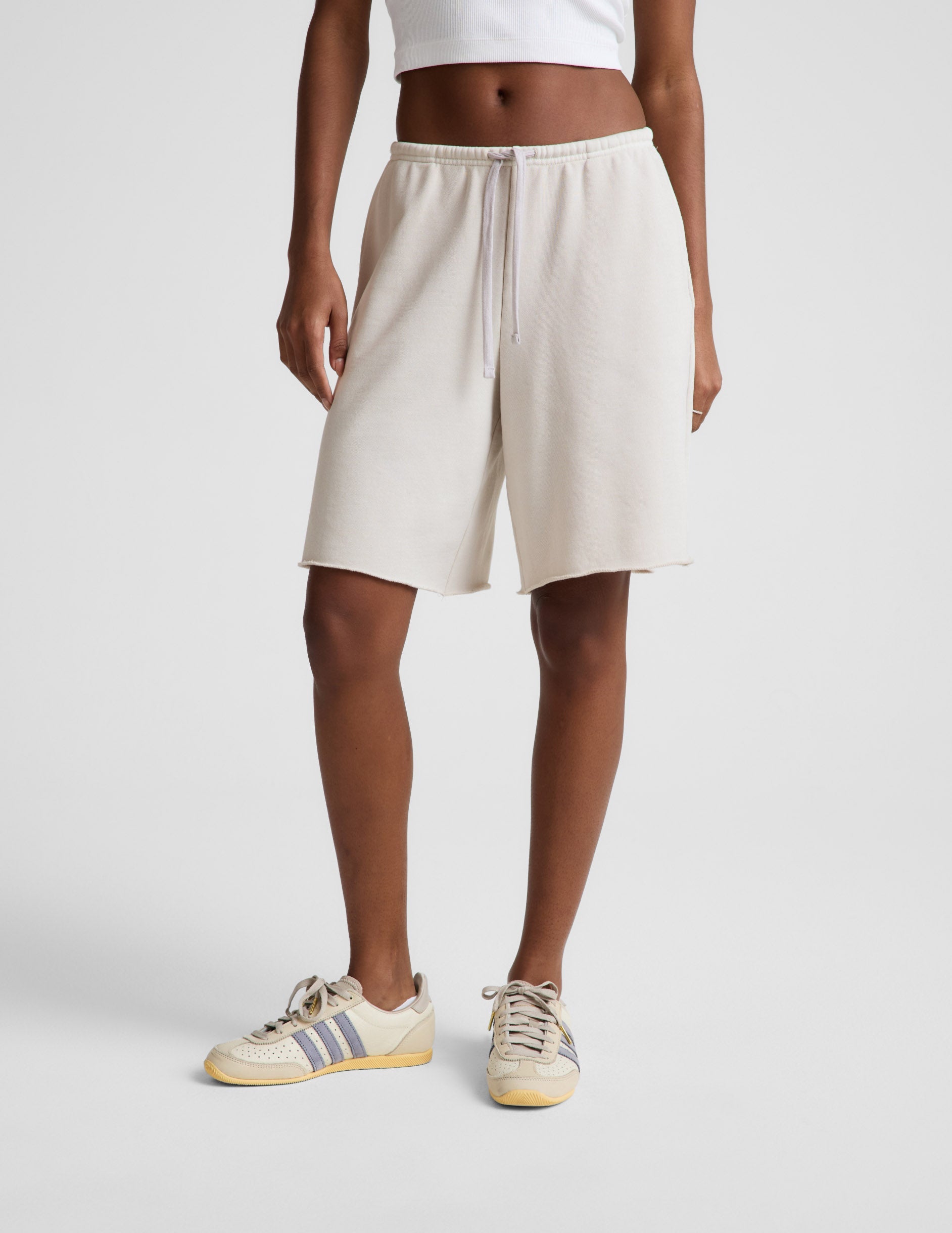 Woman wearing Beige Fade Out Low-Rise Bermuda Short™ with a raw hem, paired with a white top and cream sneakers.