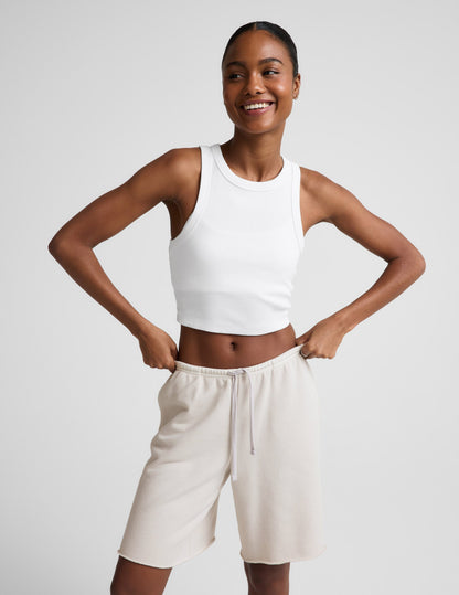 Woman wearing Beige Fade Out Low-Rise Bermuda Short™ paired with a white tank top, featuring drawstrings and a raw hem.