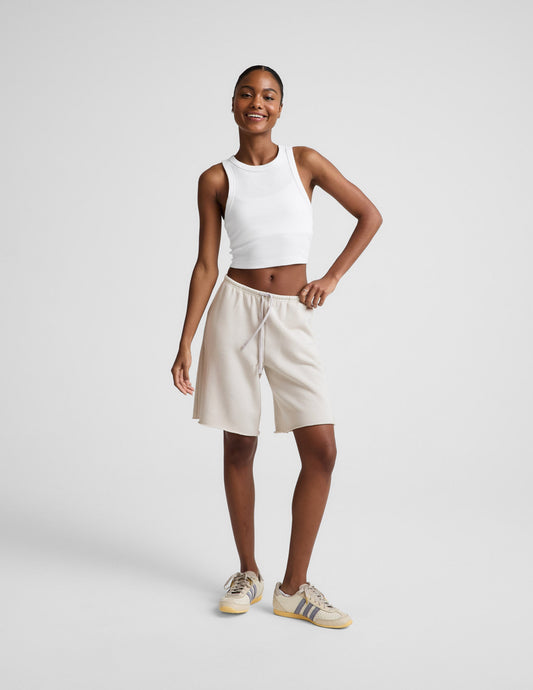 Woman wearing Beige Fade Out Low-Rise Bermuda Short™ with a raw hem and drawstring, paired with a white tank top.