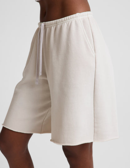 Woman wearing Beige Fade Out Low-Rise Bermuda Short™ with a drawstring and raw hem, paired with a white top.