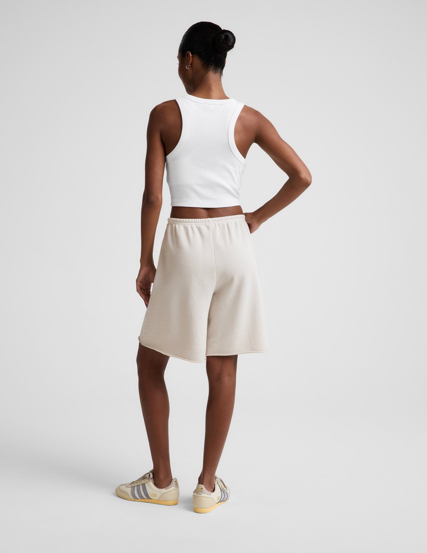 Woman wearing Beige Fade Out™ Low-Rise Bermuda Short with a white cropped tank top, rear view showing the raw hem.