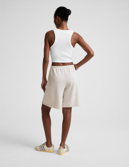 Woman wearing Beige Fade Out™ Low-Rise Bermuda Short with a white cropped tank top, rear view showing the raw hem.