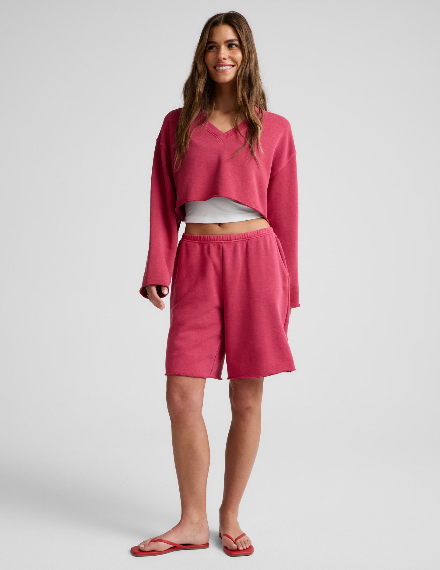 Woman wearing Pink Fade Out Low-Rise Bermuda Short™ paired with a matching cropped sweatshirt and red sandals.