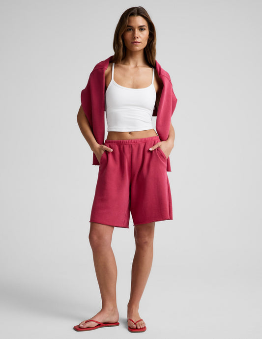 Woman wearing Pink Fade Out™ Low-Rise Bermuda Short with a raw hem, paired with a white tank top and pink sweatshirt.