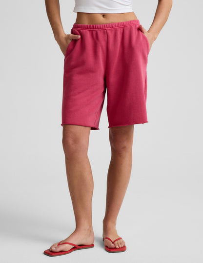 Woman wearing Pink Fade Out Low-Rise Bermuda Short with raw hem and elastic waistband, paired with a white crop top.