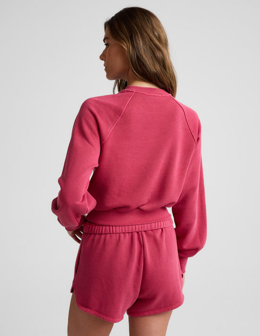 Woman wearing a red cropped sweatshirt and shorts against a plain background.