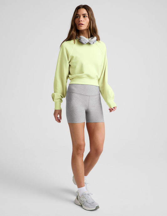Woman wearing a yellow cropped sweatshirt and gray biker shorts against a plain background.