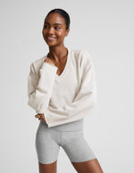 Woman wearing a white v-neck cropped sweatshirt and gray biker shorts against a plain background.