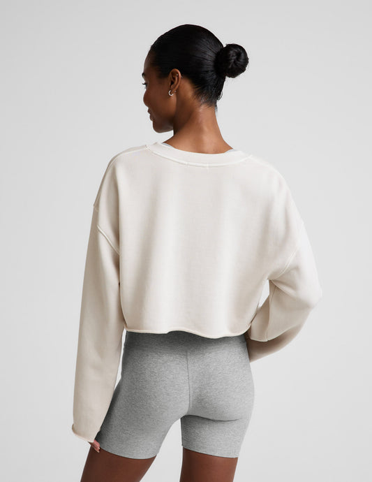Woman wearing a white v-neck cropped sweatshirt and gray biker shorts against a plain background.