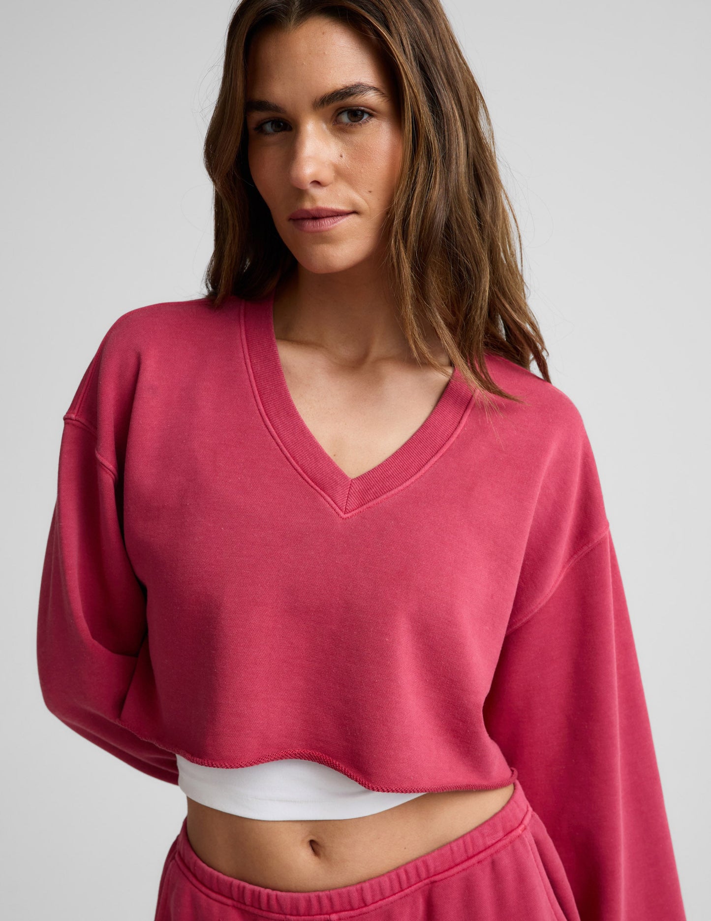 Woman wearing a red cropped long sleeve v-neck sweatshirt and shorts against a plain background.