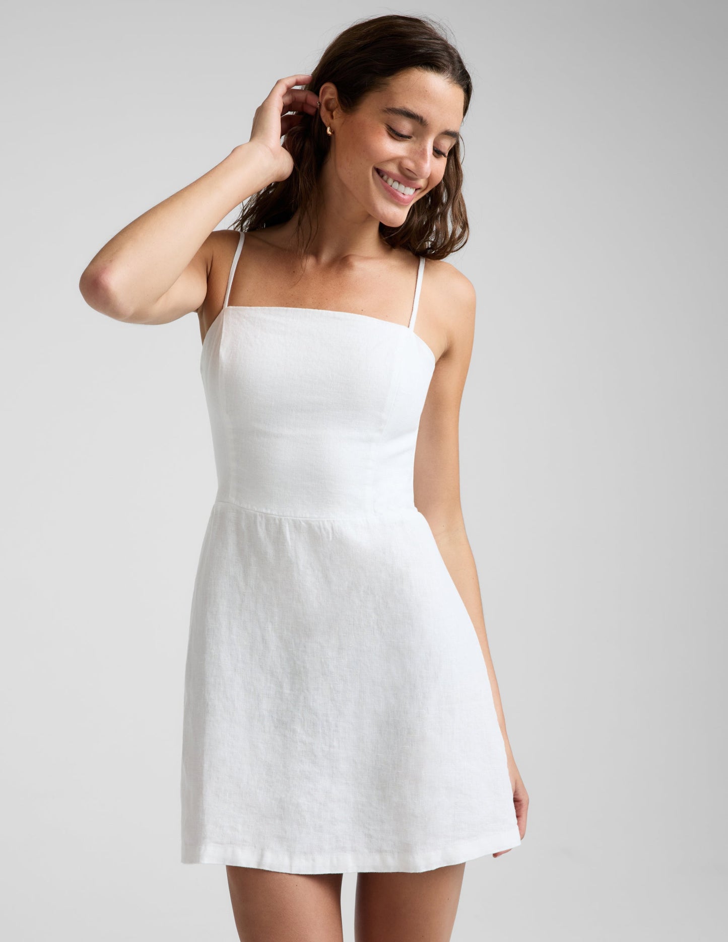 Woman wearing a white linen mini dress against a plain background.