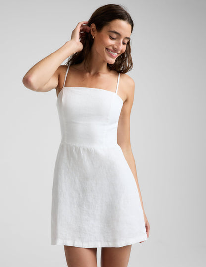 Woman wearing a white linen mini dress against a plain background.