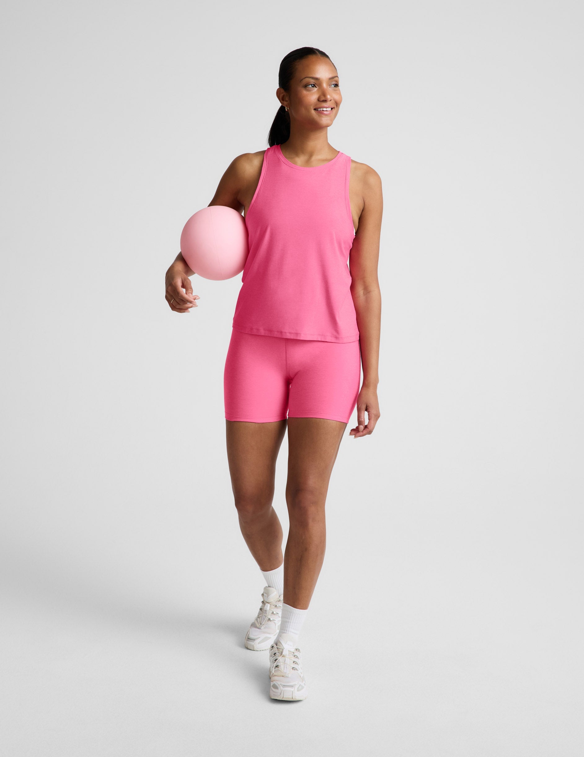 Woman wearing a pink tank top and biker shorts against a plain background.