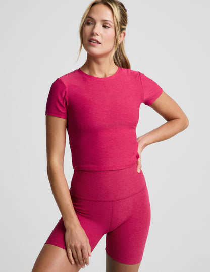 Woman wearing a red cropped lightweight t-shirt and biker shorts against a plain background.