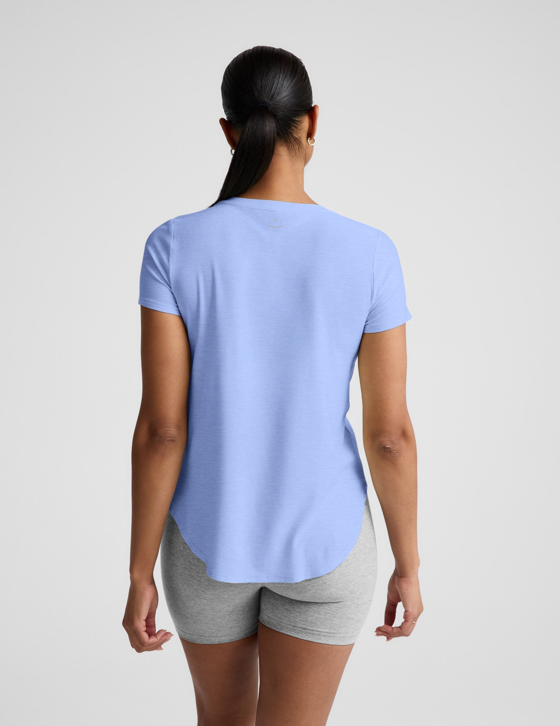 Woman wearing a light blue t-shirt and gray biker shorts against a plain background.