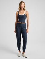 Woman wearing a blue tank top and blue joggers against a plain background.