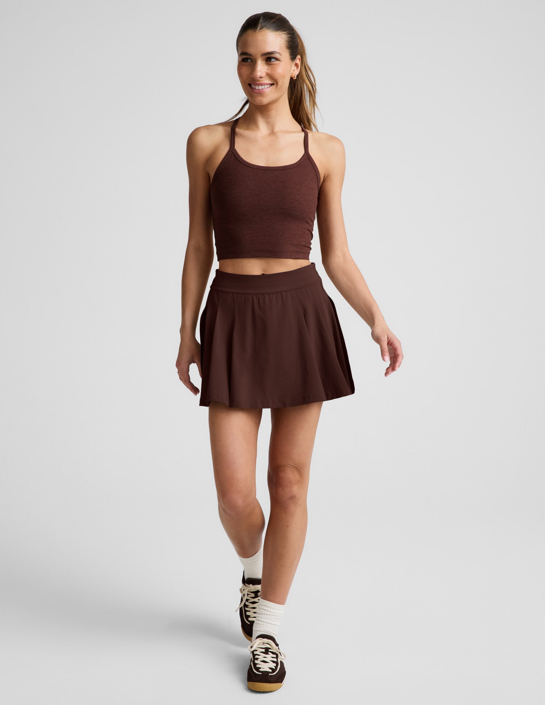Woman wearing Brown Score™ Pleated Skirt with stitch down front pleats, paired with a matching cropped tank and sneakers.