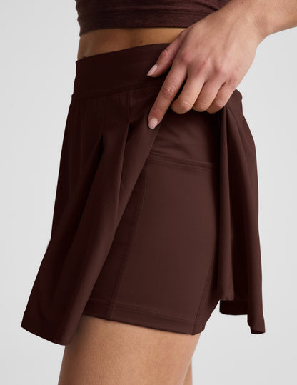 Side profile of woman wearing Brown Score Pleated Skirt™ with a brown top, showing the interior shorts and side pocket.