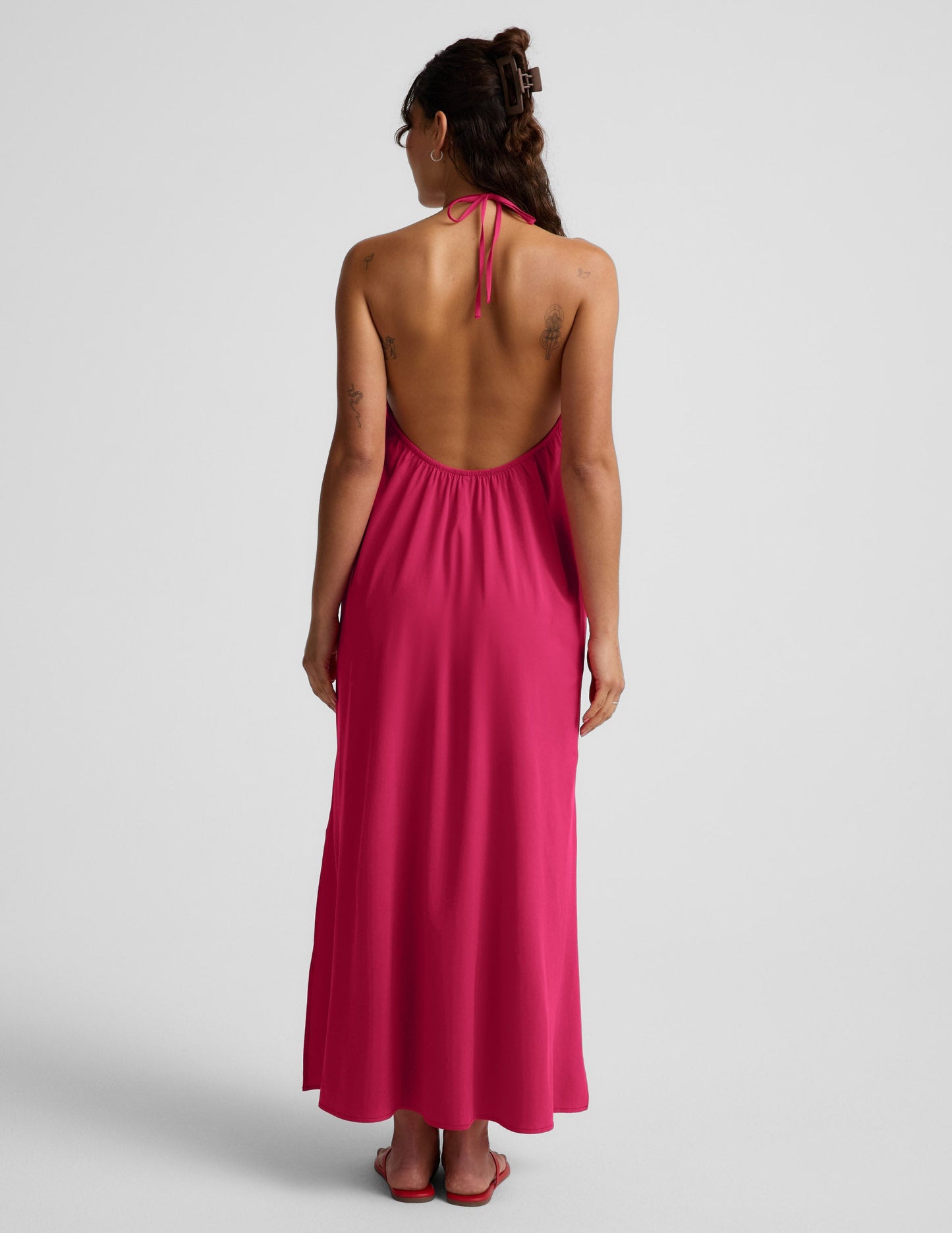 Woman wearing a red halter maxi dress with an open back against a light gray background.