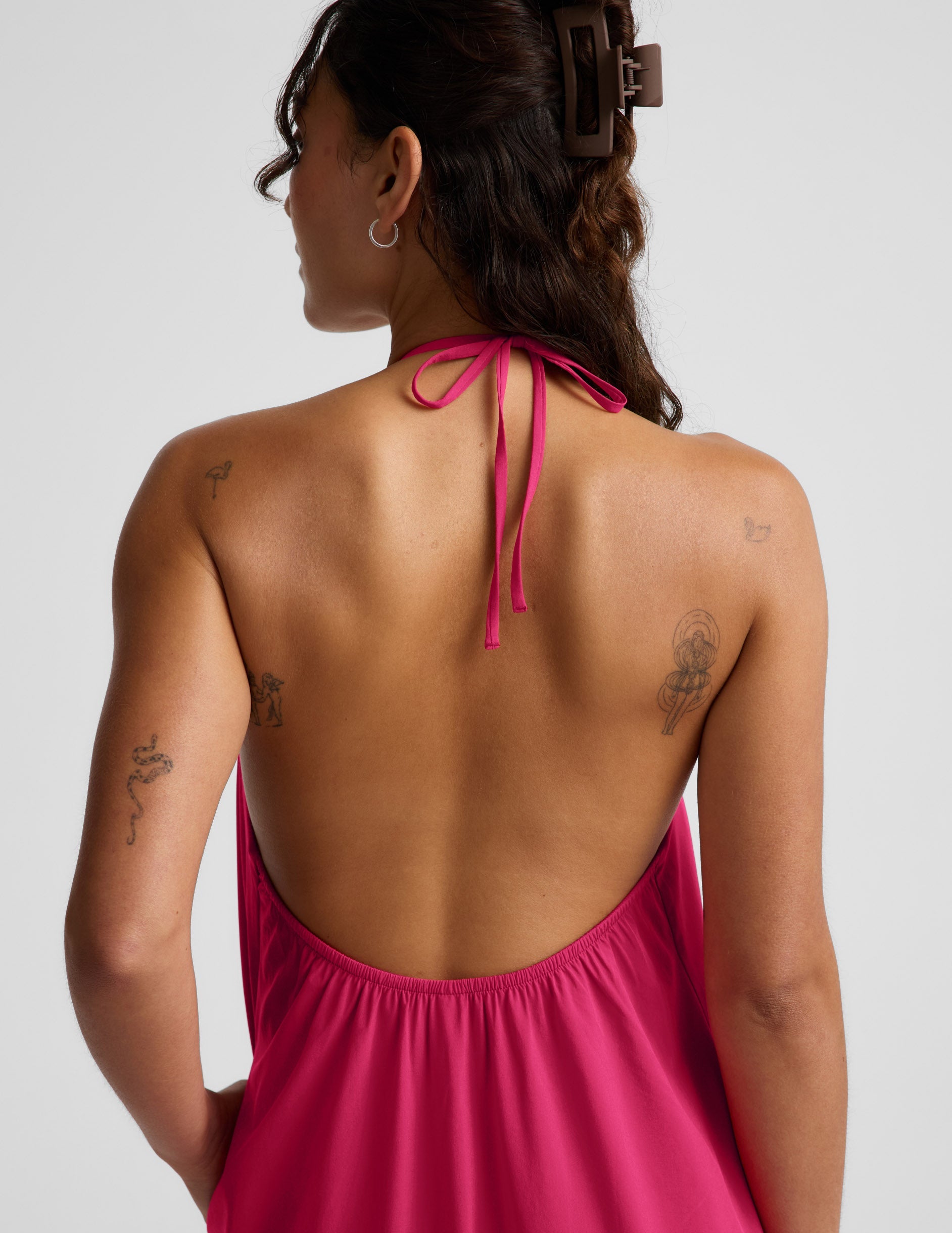 Woman wearing a red halter maxi dress with an open back against a light gray background.