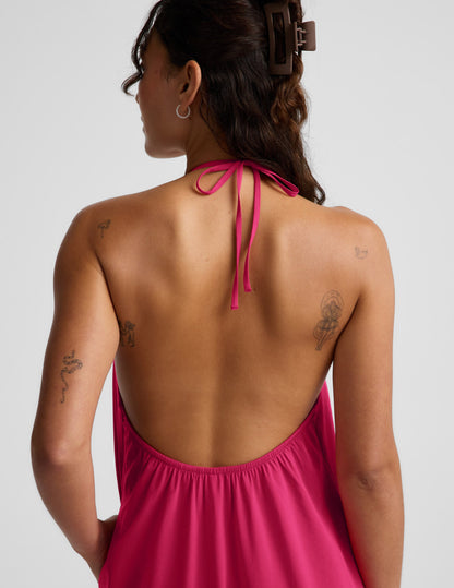 Woman wearing a red halter maxi dress with an open back against a light gray background.
