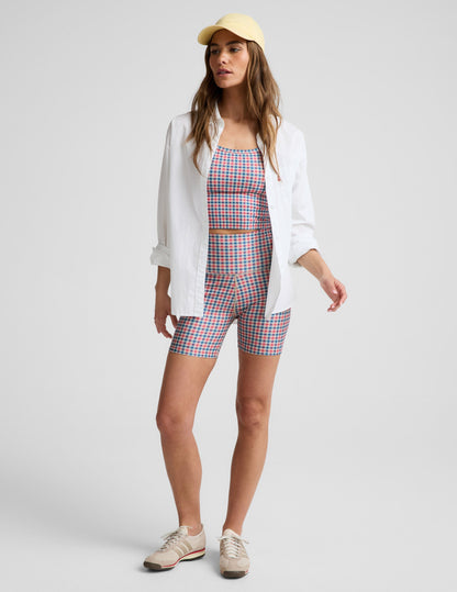 Woman wearing a red, white, and blue gingham pattern cropped tank top and biker shorts against a light gray background.