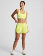 Woman wearing Yellow Solemate™ 2.5" Short featuring dolphin hems paired with a matching sports bra and white sneakers.