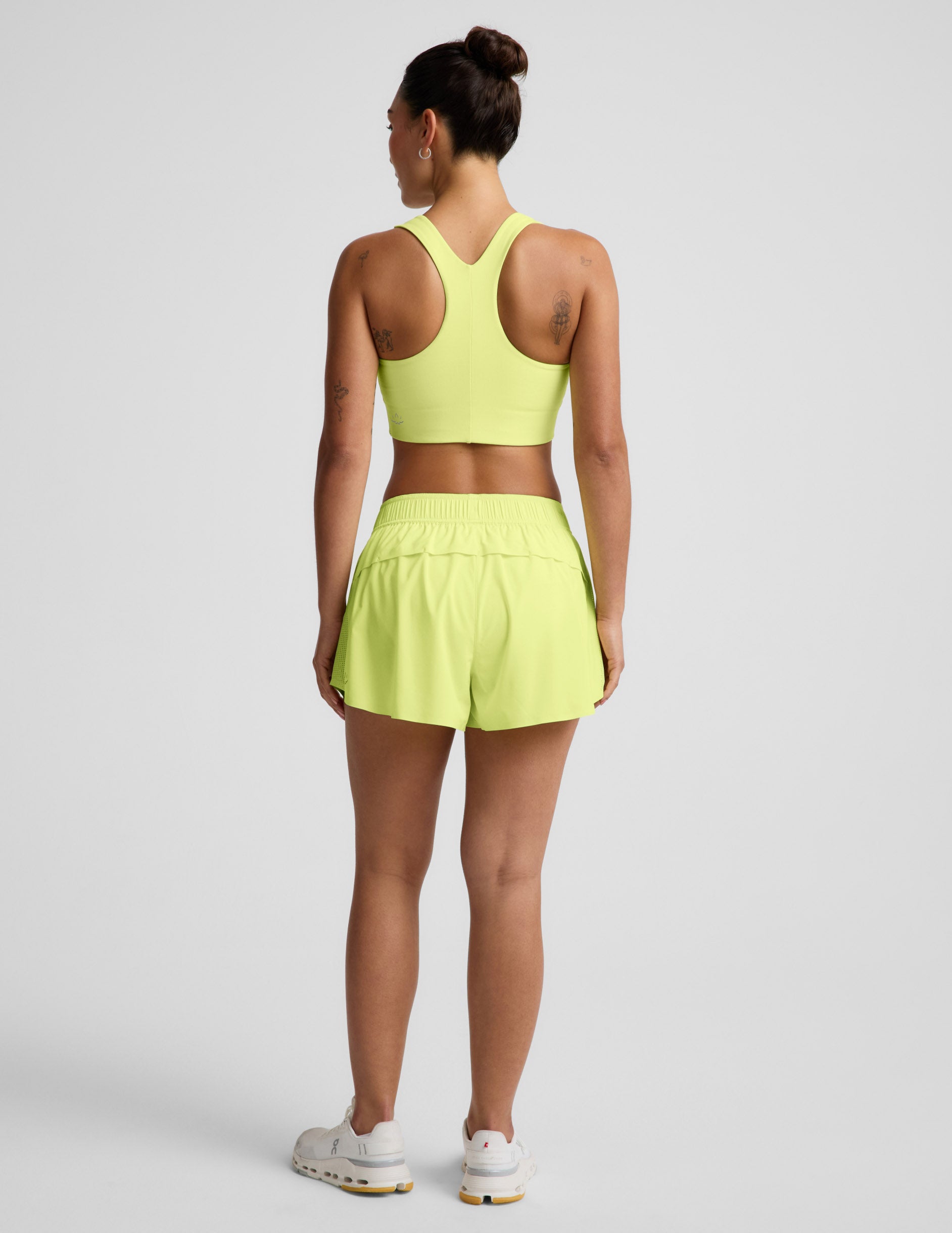 Rear view of woman wearing Yellow Solemate™ 2.5" Short with a matching sports bra and white sneakers.