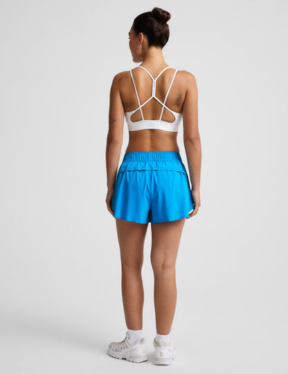 Woman wearing Blue Solemate™ 2.5" Short from a rear view, paired with a white sports bra and white sneakers.