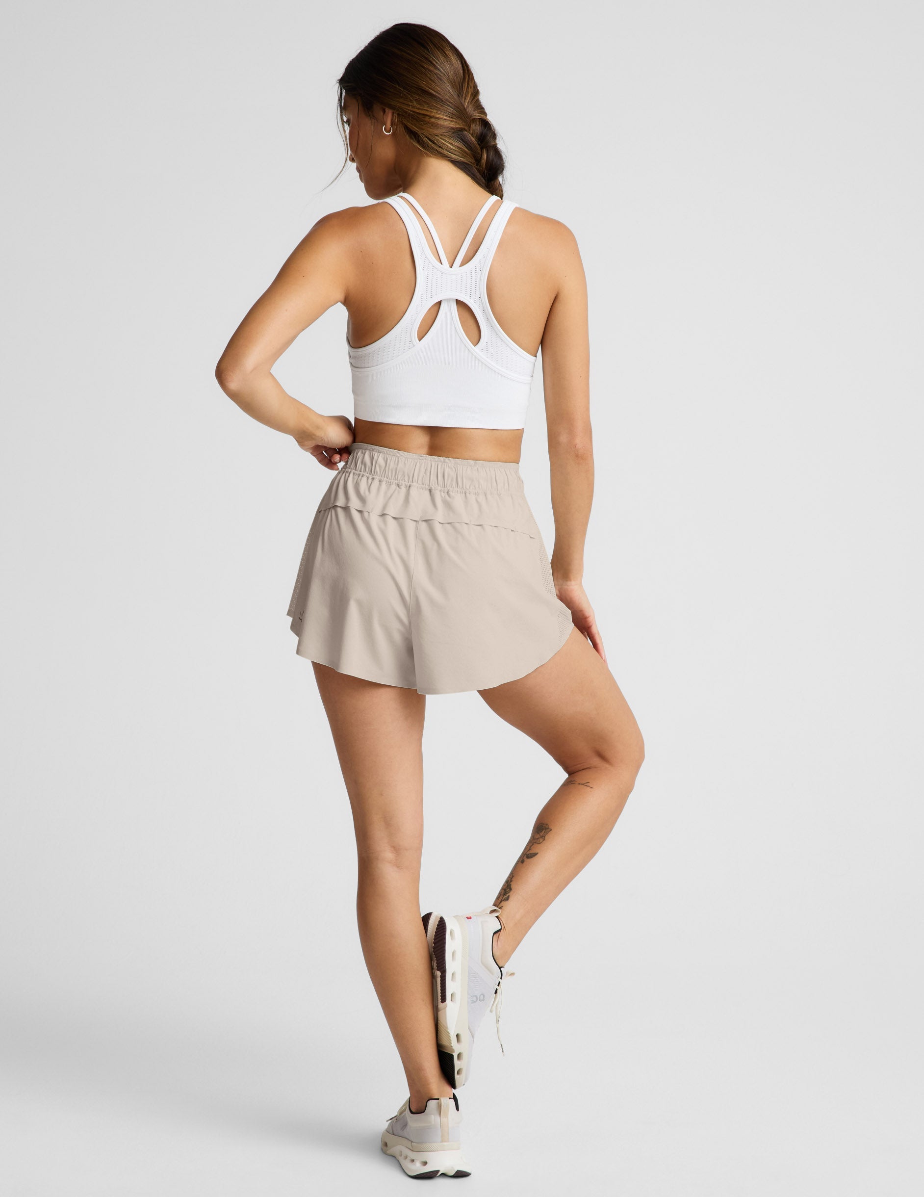 Woman wearing Beige Solemate™ 2.5" Short in a rear view, featuring a vented back panel and paired with a white sports bra.